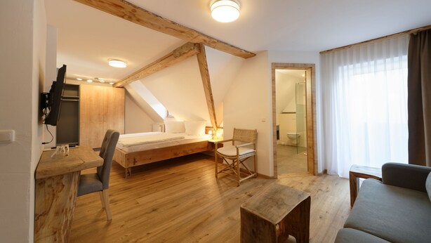 Un dormitorio con techo de madera, una cama, un escritorio con silla y una ventana con cortinas.