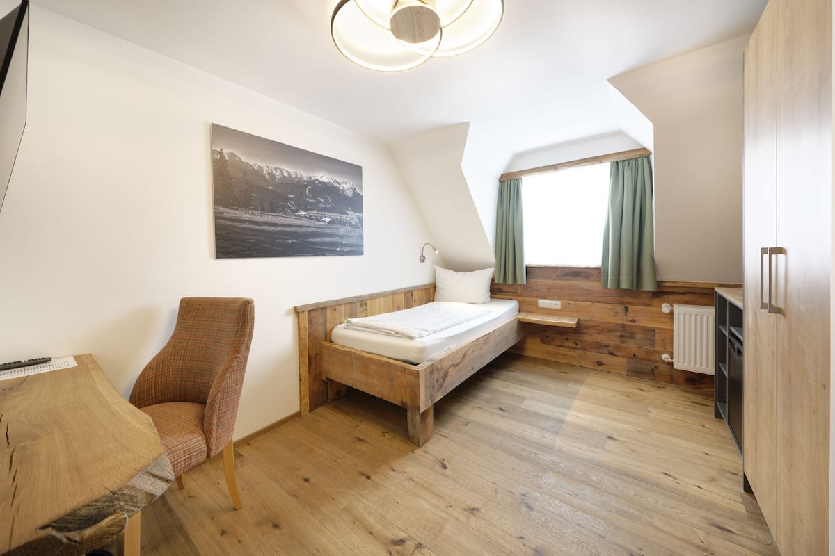 A bedroom with a wooden bed, a chair, a desk, and a painting on the wall.
