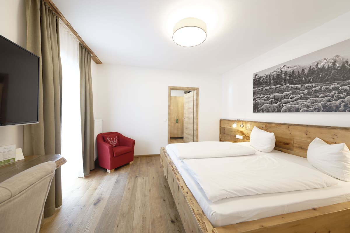 A hotel room with a wooden bed, a red chair, a flat-screen TV, and a large painting of sheep on the wall.