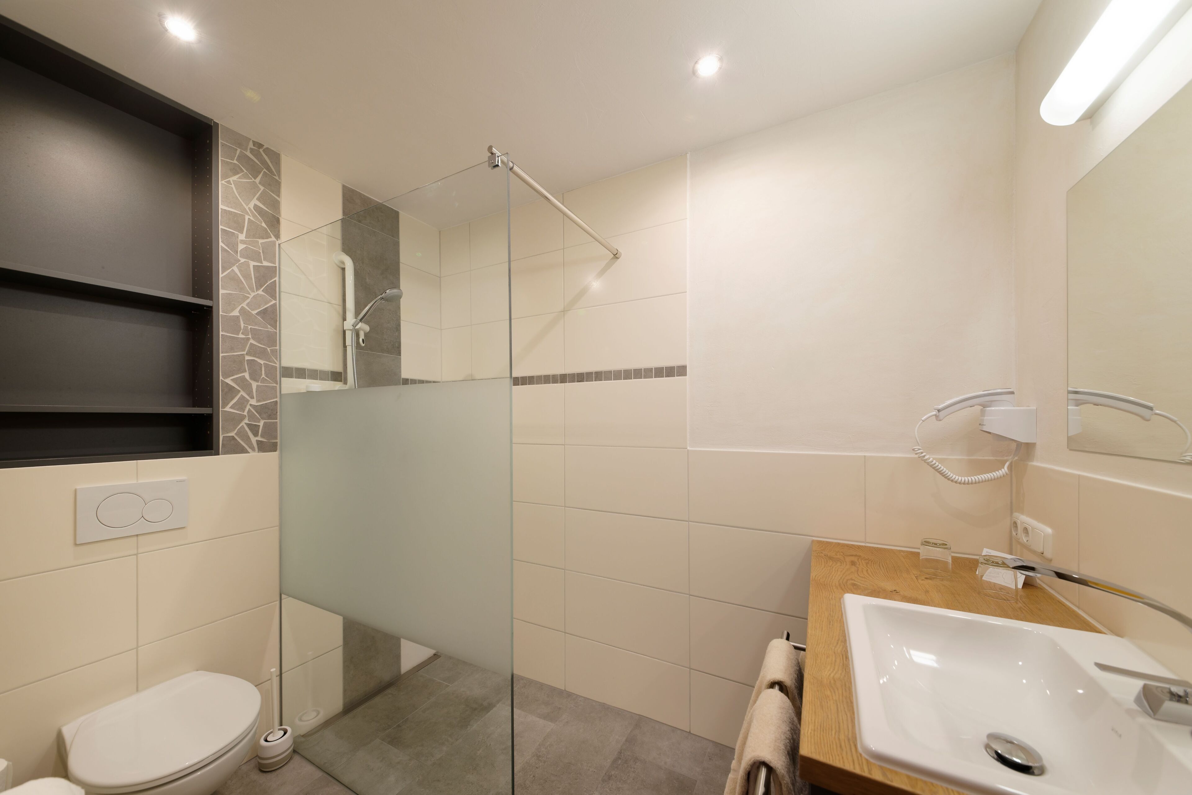 Un baño moderno con ducha envuelta en vidrio, tocador de madera y inodoro blanco.