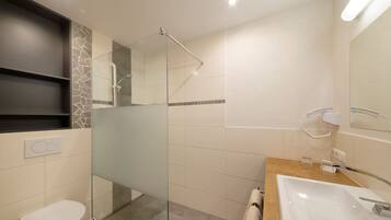 Un baño moderno con ducha envuelta en vidrio, tocador de madera y inodoro blanco.