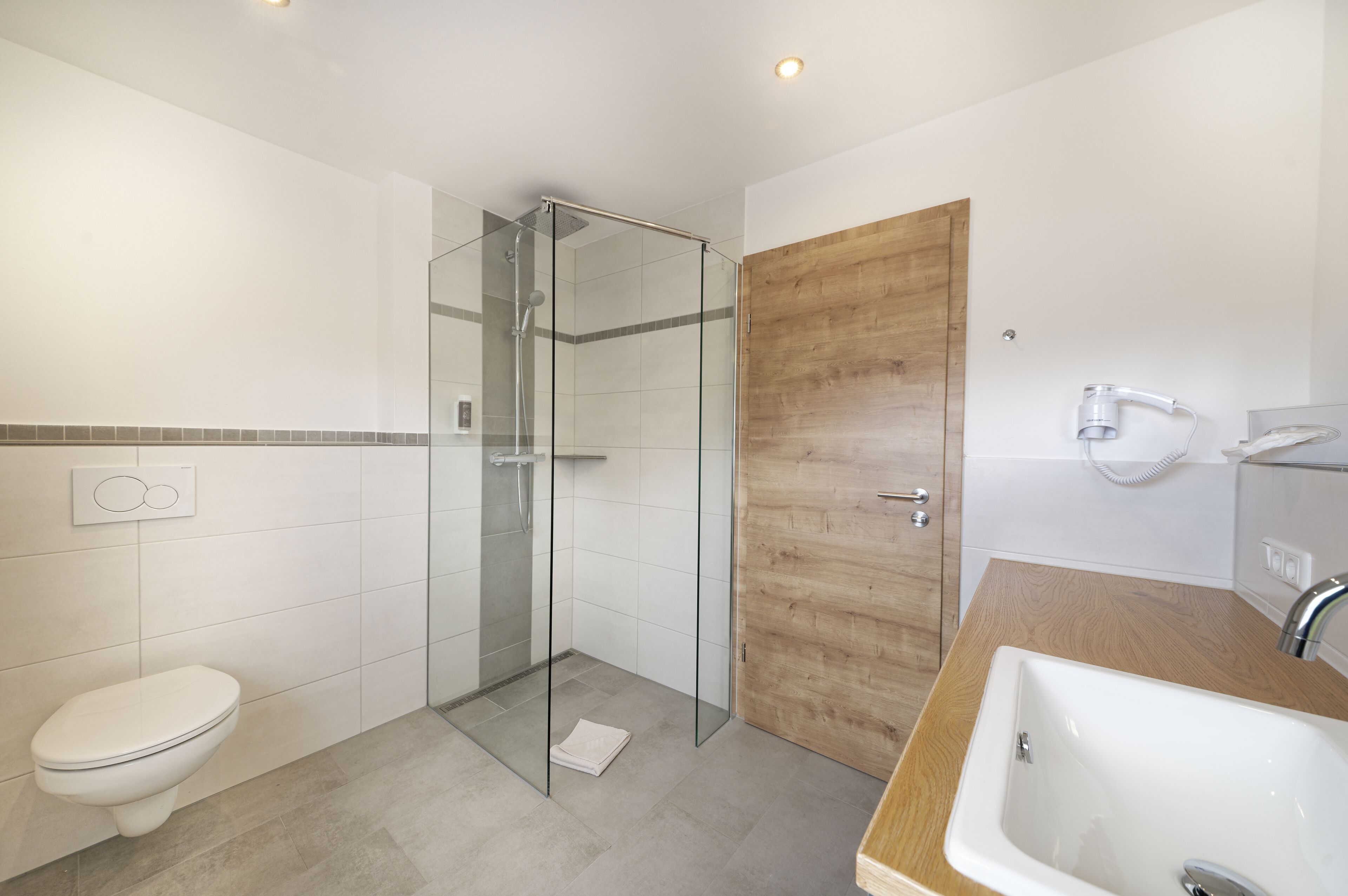 A modern bathroom with a glass-enclosed shower, a wooden door, and a sink with a mirror.