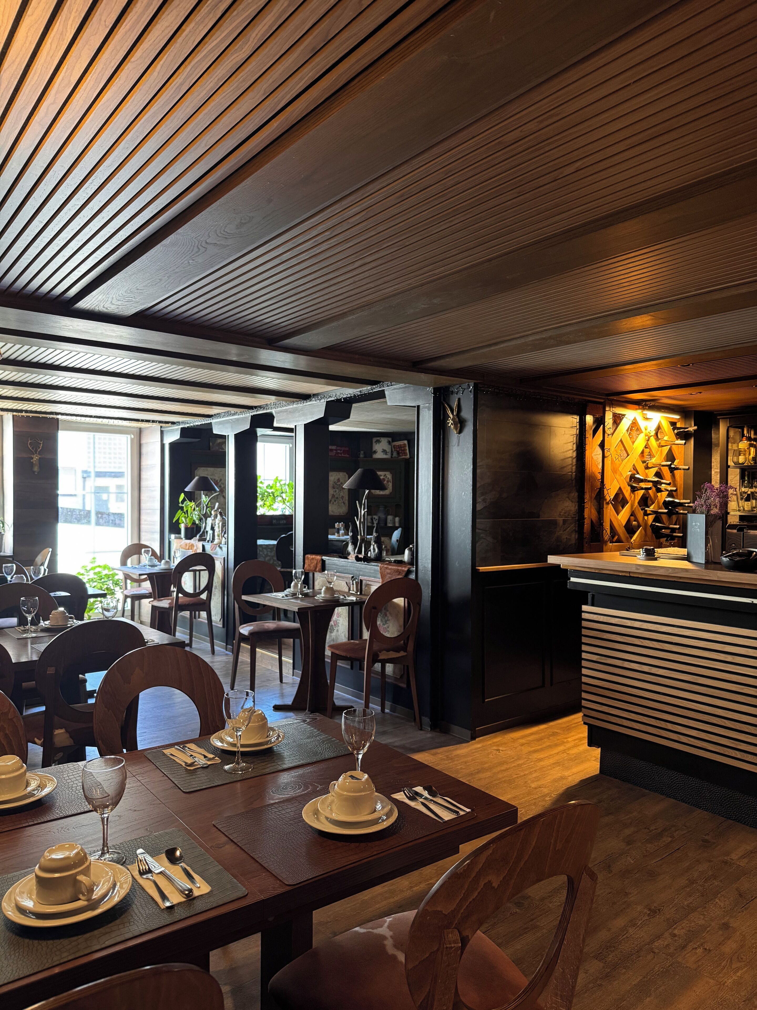 Een restaurant met houten balken in het plafond, gedekte tafels en een bar met flessen.