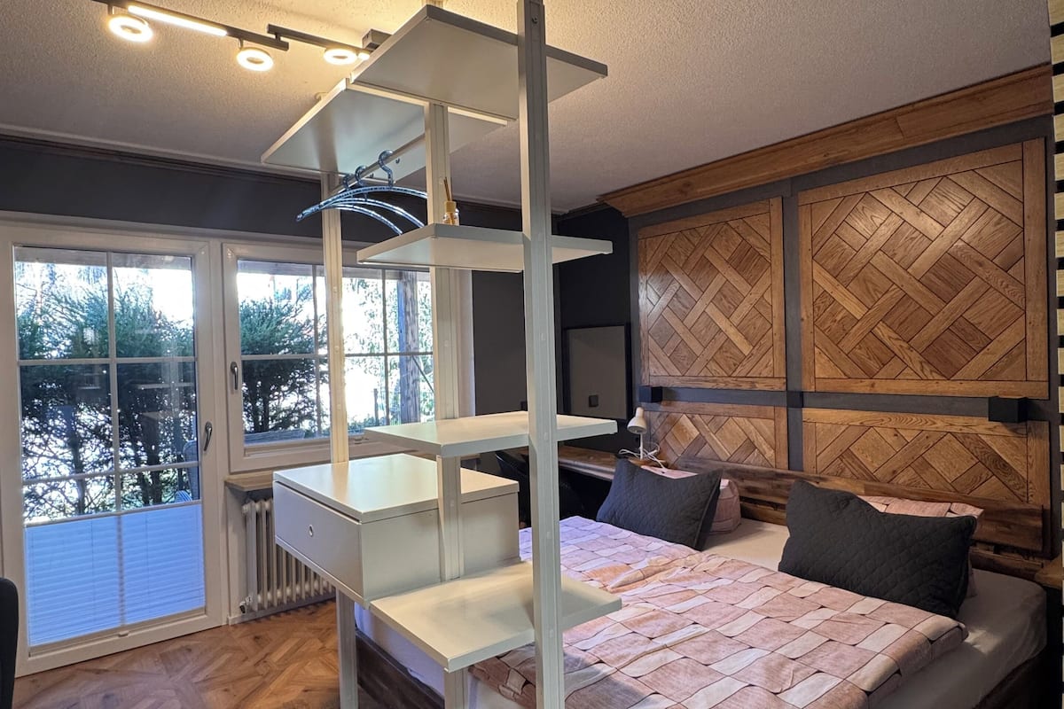 A modern bedroom with a bed, a white desk, and a built-in shelving unit.