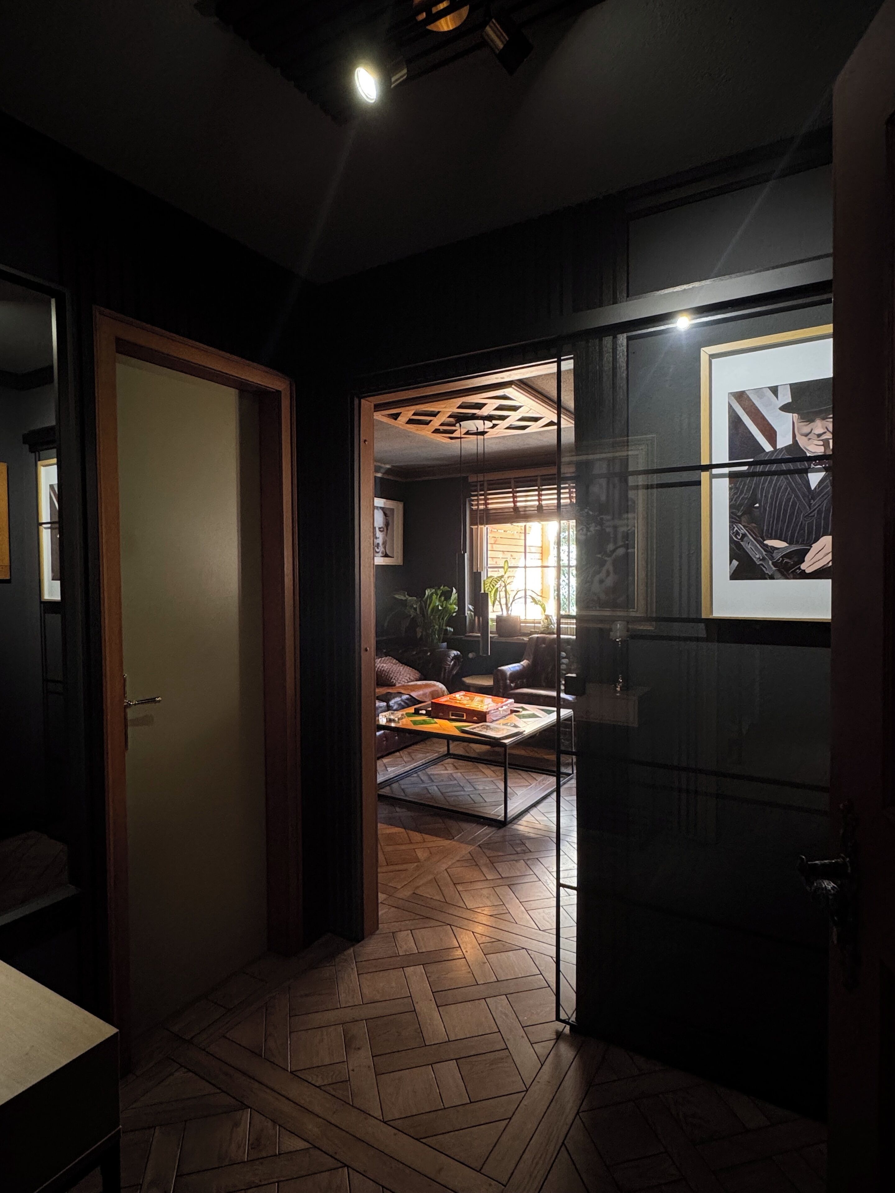 A hallway with a herringbone floor leading to a living area with a sofa, coffee table, and a framed picture on the wall.