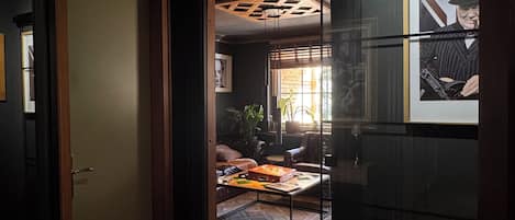 A hallway with a herringbone floor leading to a living area with a sofa, coffee table, and a framed picture on the wall.