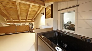 A modern bathroom with a black bathtub, white tiles, and wooden ceiling beams. - Freiraum Zentral (Garmisch-Partenkirchen)