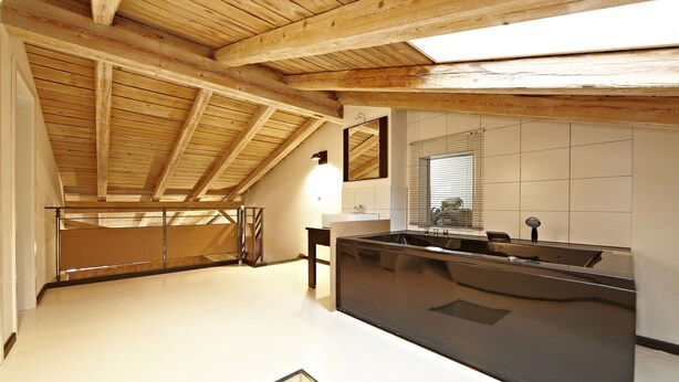 A modern kitchen with a large black countertop, wooden beams on the ceiling, and a window with blinds. - Freiraum Zentral (Garmisch-Partenkirchen)