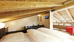 A bedroom with a wooden ceiling, a bed with white bedding, a red chair, and a TV on the wall. - Freiraum Zentral (Garmisch-Partenkirchen)