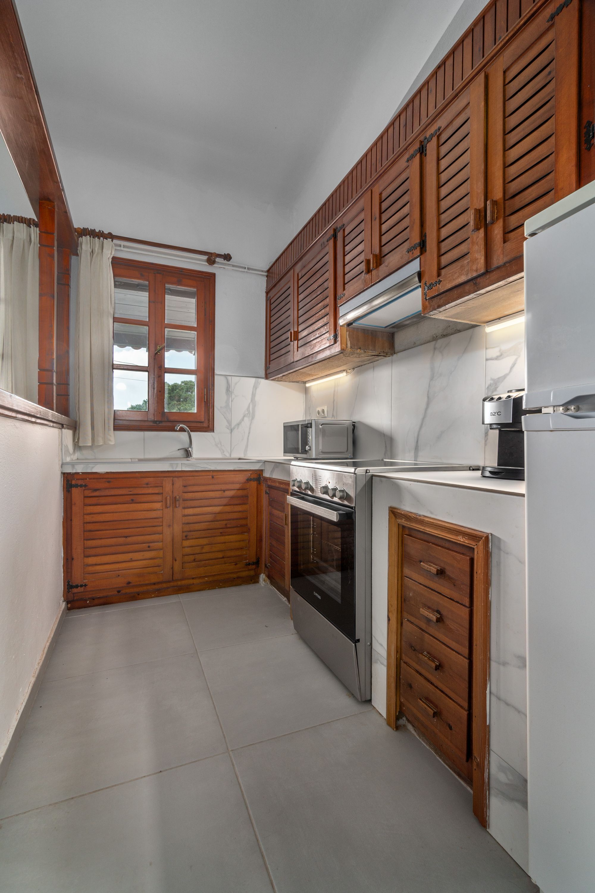 A compact kitchen with wooden cabinets, a built-in oven, a microwave, and a refrigerator.