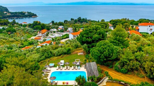 Un resort costero con piscina, vegetación exuberante y casas con tejados rojos.