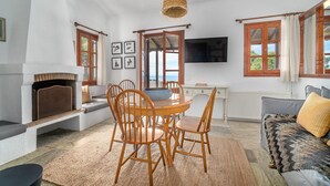 Una sala de estar acogedora con chimenea, un comedor con sillas de madera, un sofá y un televisor montado en la pared.