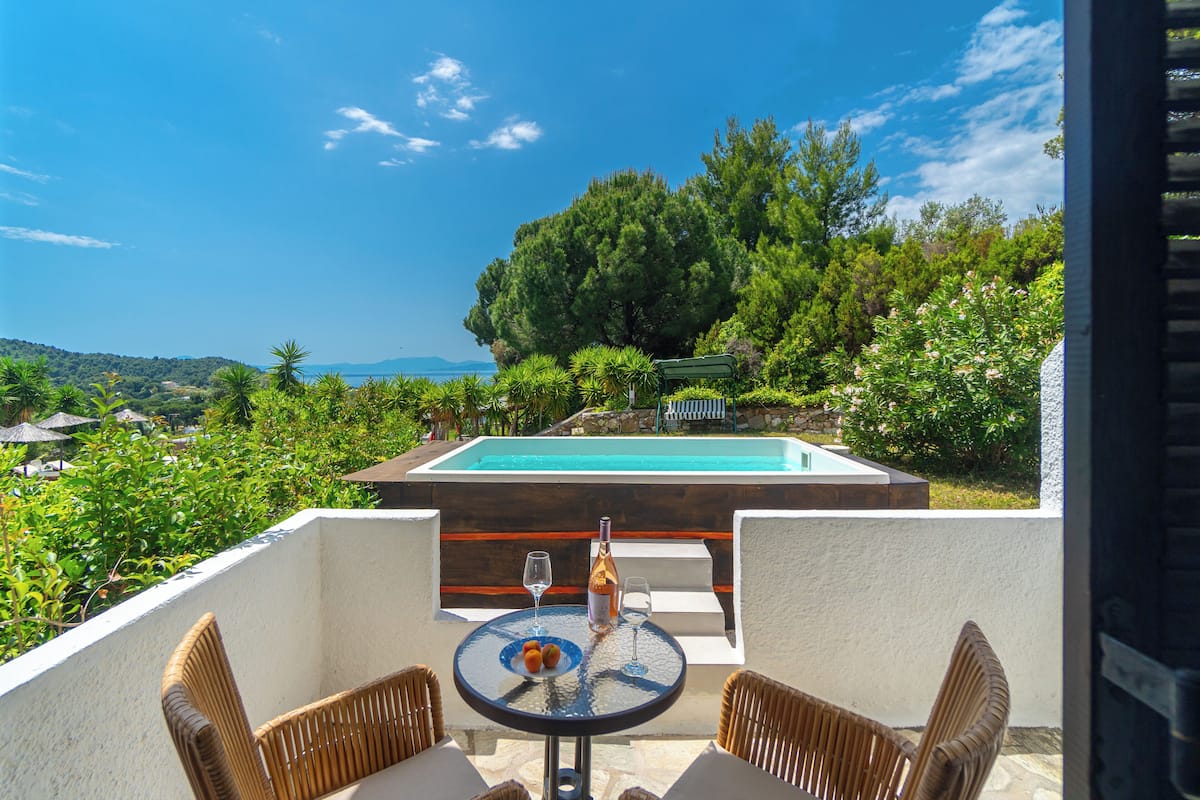 Una terraza con piscina, sillas de mimbre y una mesa con una botella y vasos.