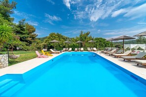 Une piscine entourée de verdure et d’arbres, avec des chaises longues et des parasols.
