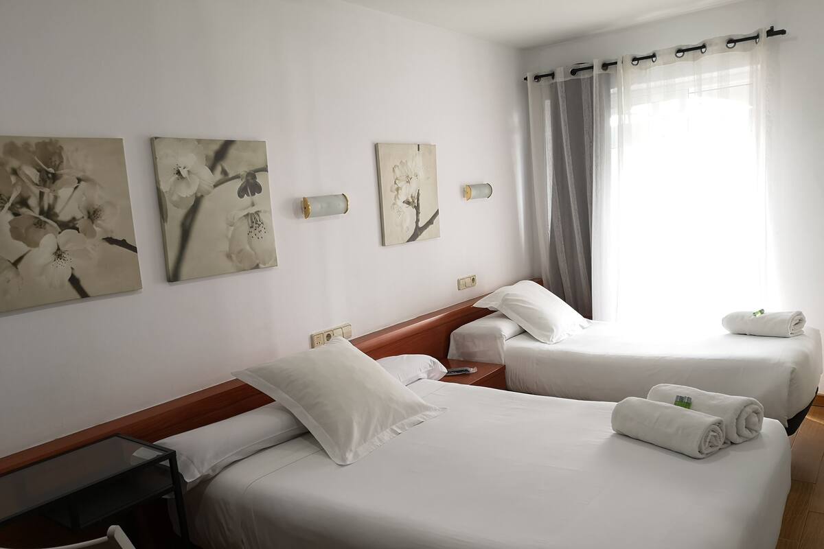 Una habitación de hotel con dos camas, un cabecero de madera, una mesita y cuadros en las paredes.