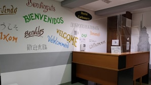 A reception desk with a wall displaying multilingual welcome signs. - Hostal Carbonara (A Coruña)