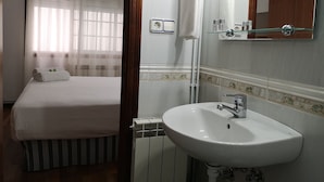 A hotel room with a bed, a bathroom with a sink, and a mirror. - Hostal Carbonara (A Coruña)