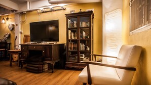 Una sala de estar acogedora con piso de madera, televisor, estantería y un sillón cómodo.