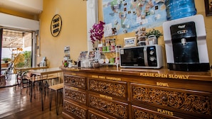 Mostrador de restaurante con una máquina de café, un dispensador grande de agua y una pared decorada con fotos y notas.