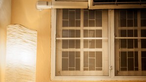 Una habitación con una única silla blanca, una ventana con diseño de cuadrícula y un equipo de aire acondicionado sobre la ventana.