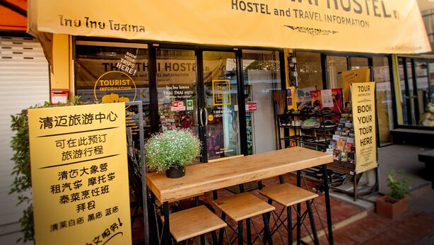 Un hostal tailandés con un letrero, asientos al aire libre y una pequeña planta en maceta.