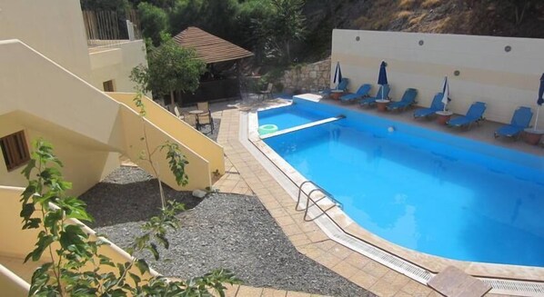 Piscina con sillones de descanso y una pequeña zona cubierta para sentarse.