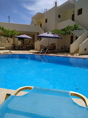 Piscina con agua azul cristalina, rodeada de mobiliario exterior y sombrillas.