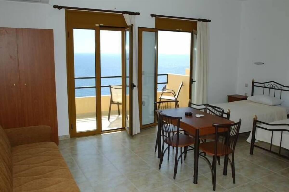 A room with a balcony, a dining table, two beds, and a sofa.