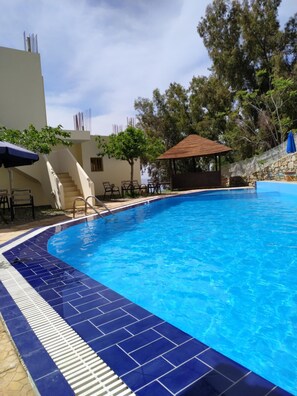Una piscina con borde de azulejos azules, una zona de estar cubierta y una escalera que conduce a un nivel superior.