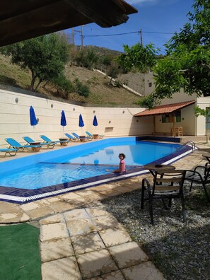 A swimming pool with blue tiles, surrounded by lounge chairs and umbrellas.