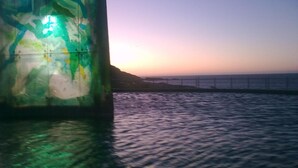 A pier with a green structure, calm water, and a sunset in the background. - Pension Las Rias (A Coruña)