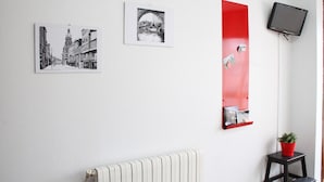 A room with a radiator, a red vertical mirror, and two black-and-white photographs on the wall. - Pension Las Rias (A Coruña)