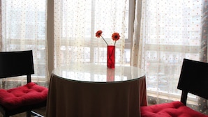 A round glass table with a red cushion, two black chairs, and a red vase with flowers. - Pension Las Rias (A Coruña)