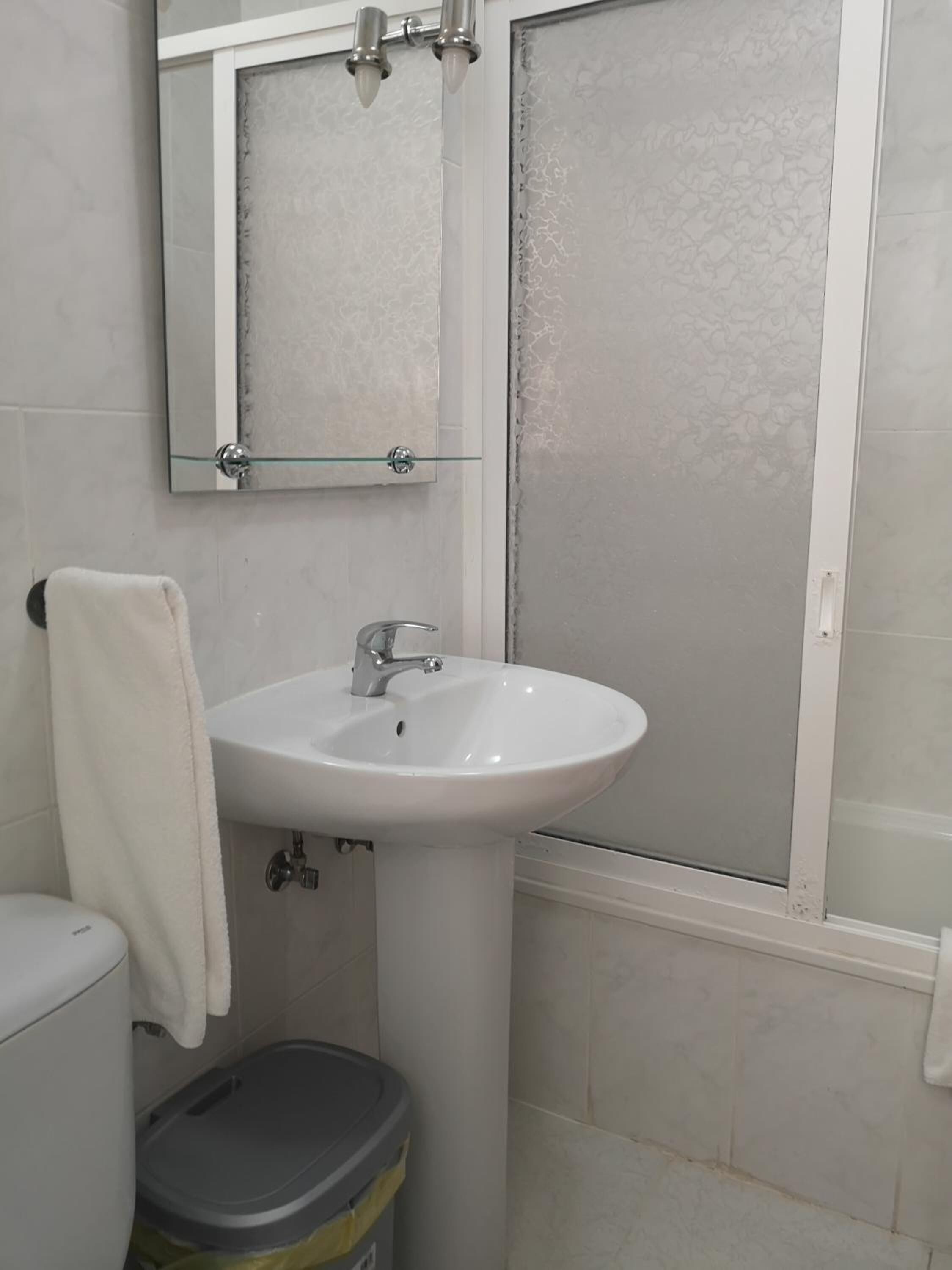 Un baño con lavamanos blanco, espejo y cabina de ducha.