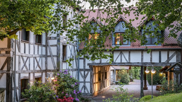 Une maison traditionnelle à colombages, avec un chemin pavé et un jardin agrémenté de plantes à fleurs.