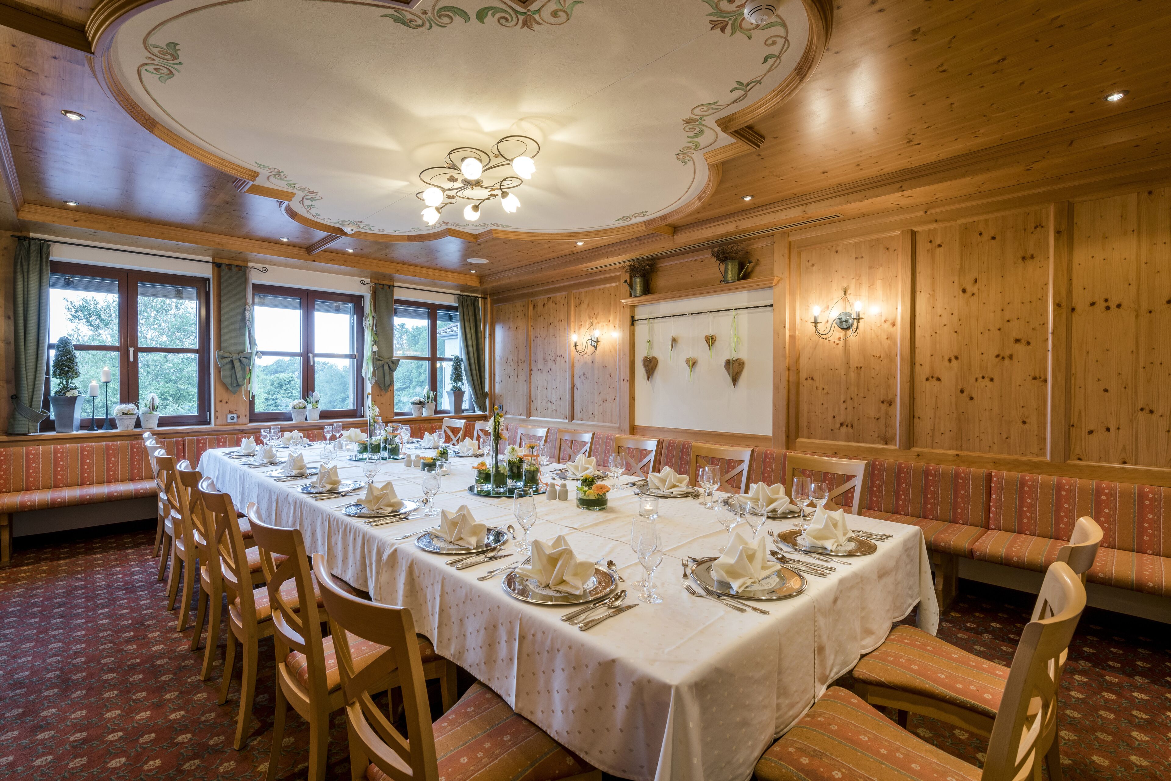 A dining room with a long table set for a meal, wooden paneling, and a large window with a view of trees.