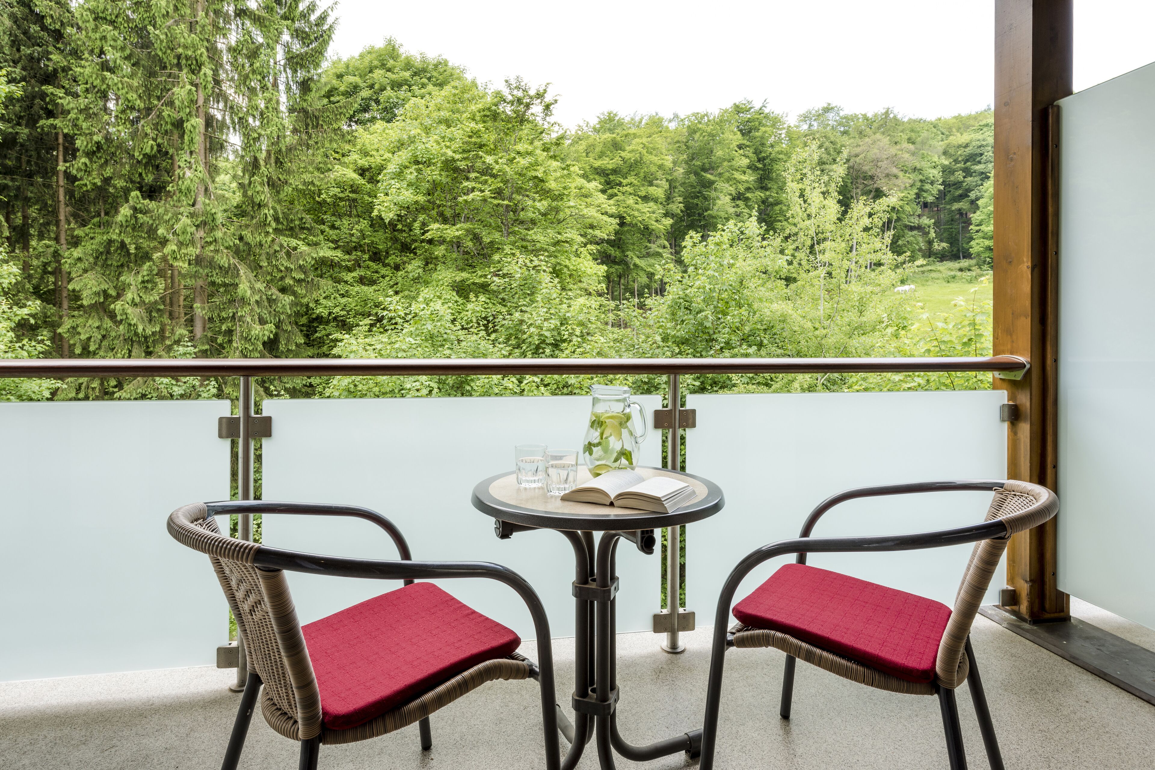 A balcony with two wicker chairs and a small table, a book, and a pitcher of water.