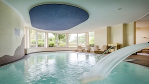 Une piscine intérieure agrémentée d’une cascade, de grandes fenêtres et de chaises longues.