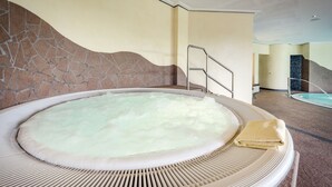 Un bain à remous avec un mur de pierres en arrière-plan, une échelle en métal et une piscine au loin.