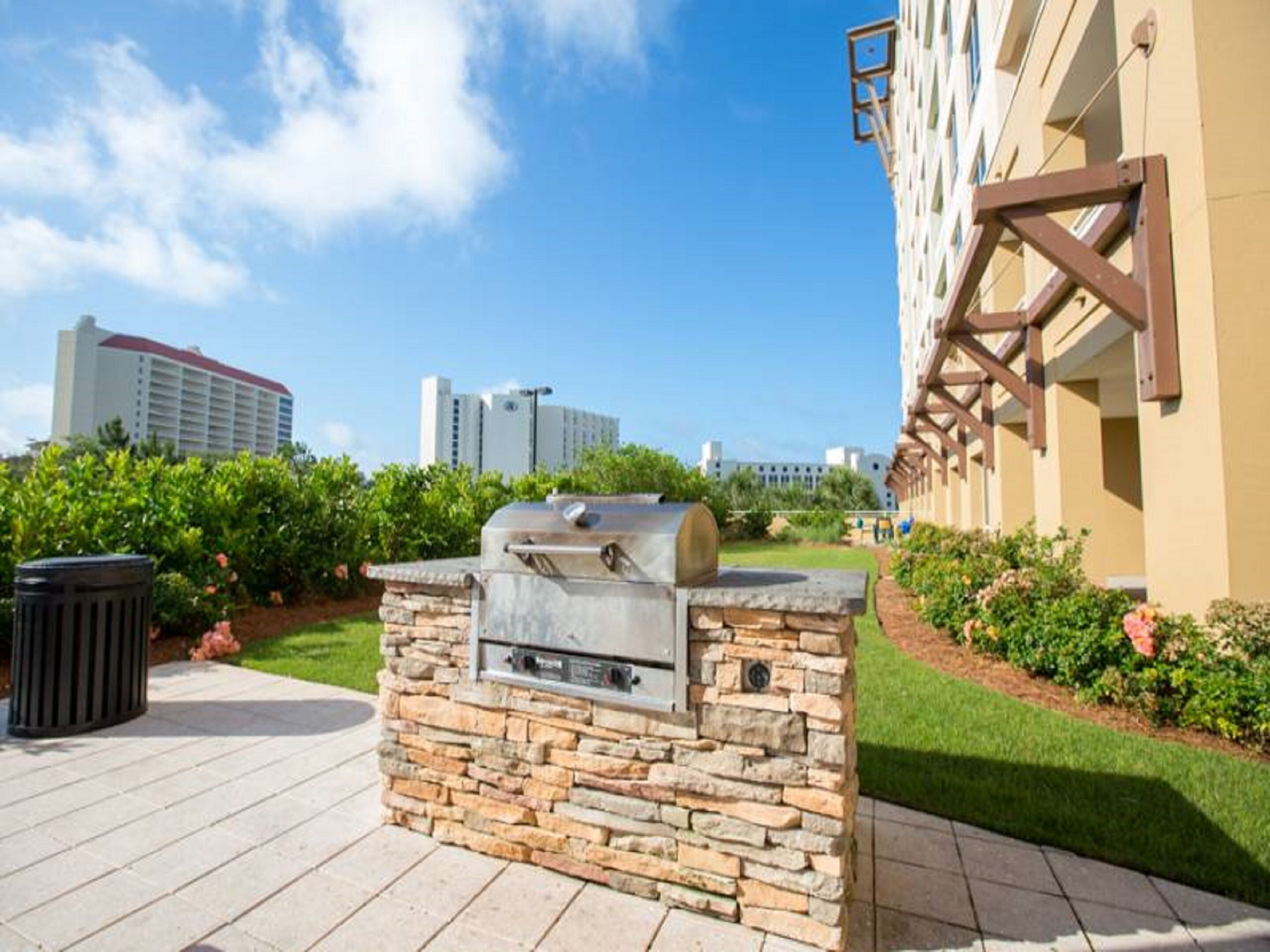 An outdoor grill area with stone walls, a paved walkway, and a building in the background.