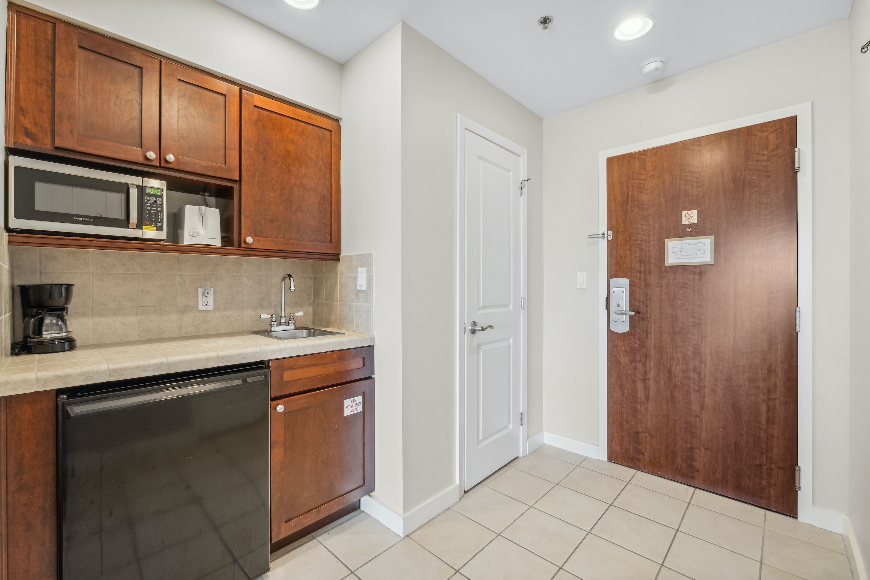 A compact kitchen with wooden cabinets, a microwave, a toaster, and a dishwasher.