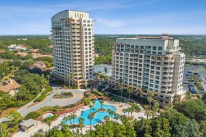 Un hotel moderno de gran altura con varias plantas, piscina y abundante vegetación.