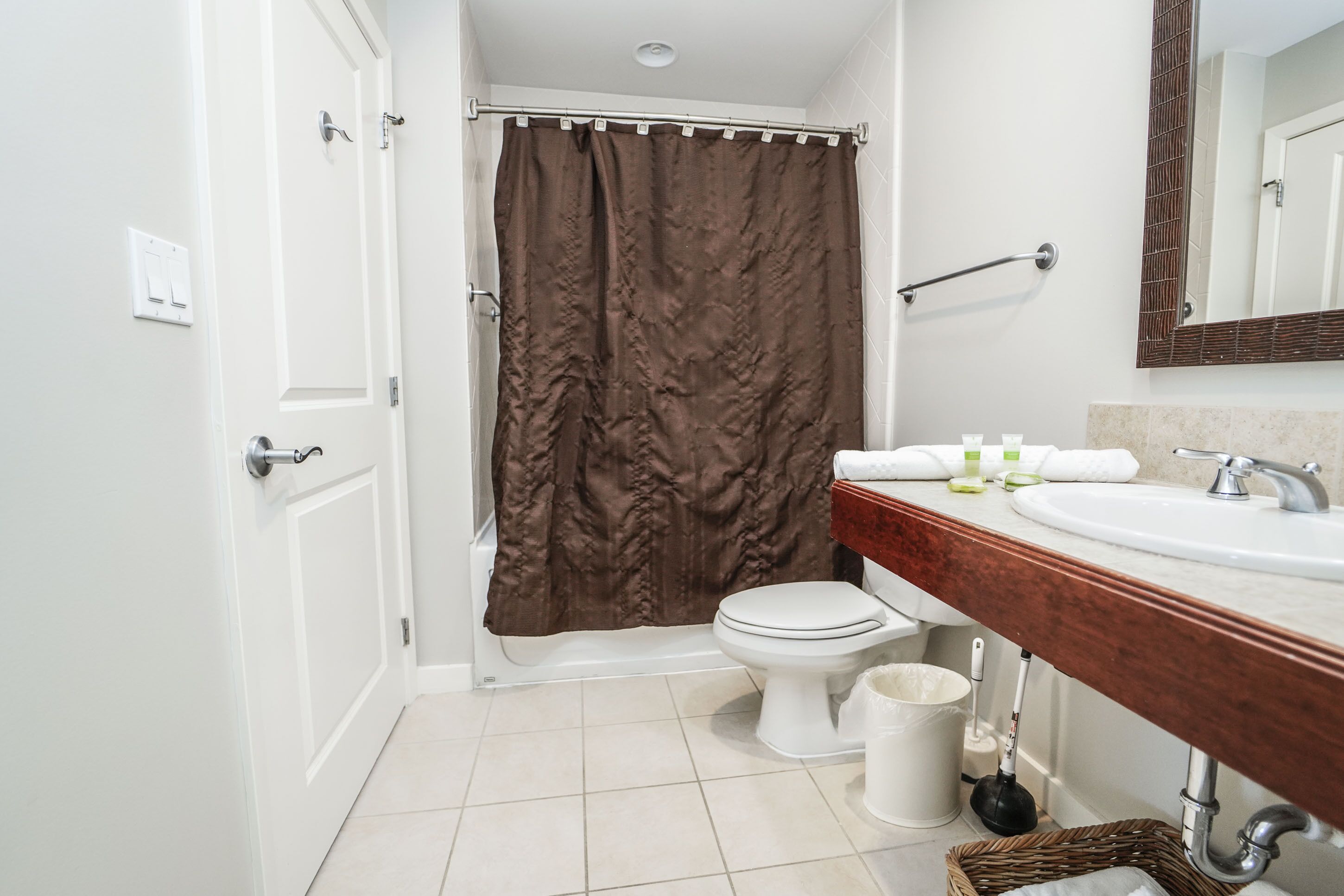 A bathroom with a white toilet, a brown shower curtain, a white sink with a wooden countertop, and a mirror above the sink.