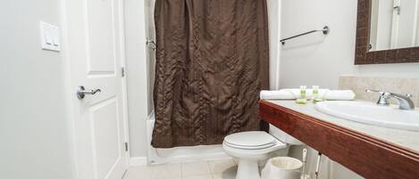 A bathroom with a white toilet, a brown shower curtain, a white sink with a wooden countertop, and a mirror above the sink.
