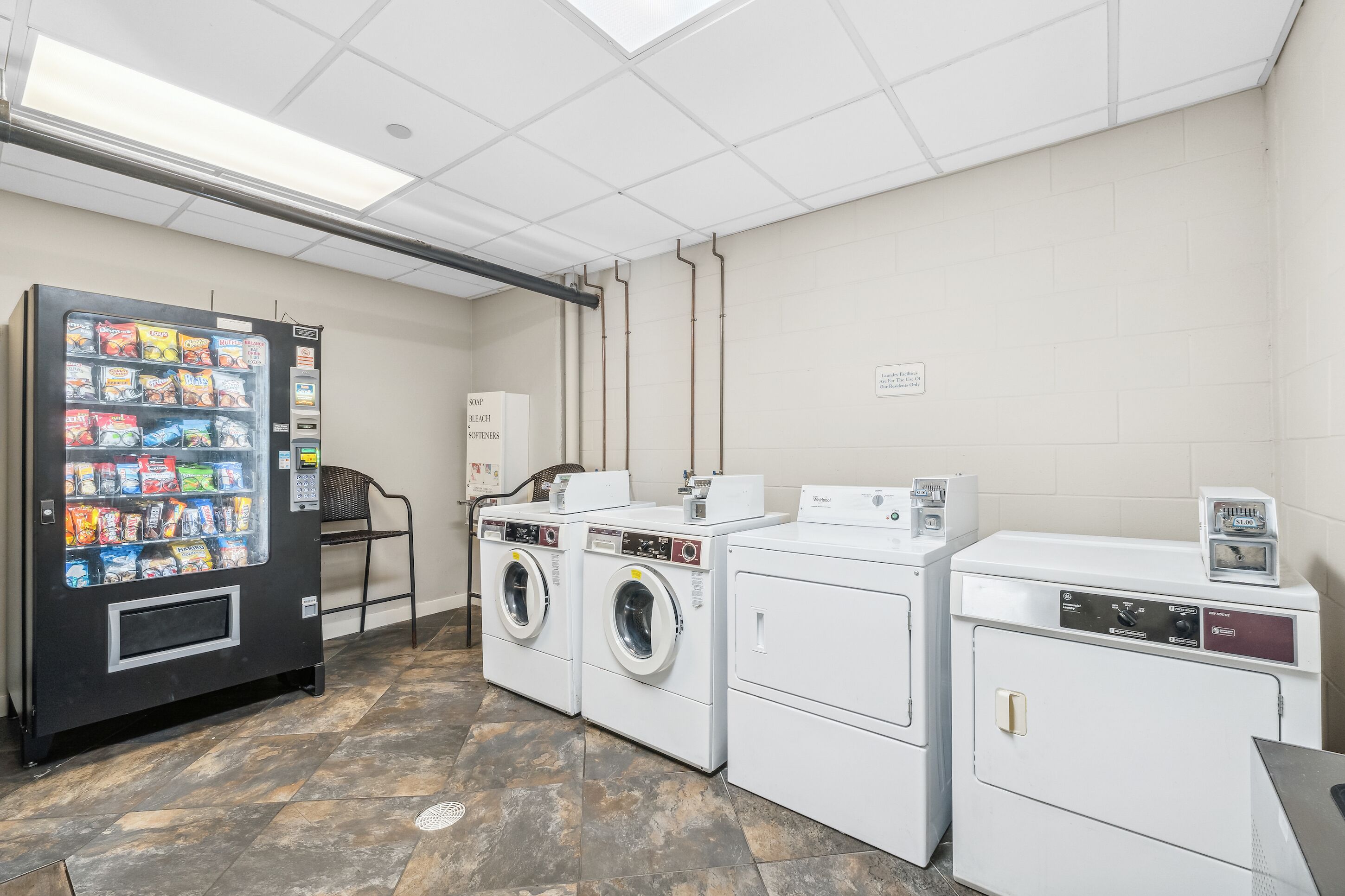 A laundry room with a vending machine, two washing machines, and a dryer.