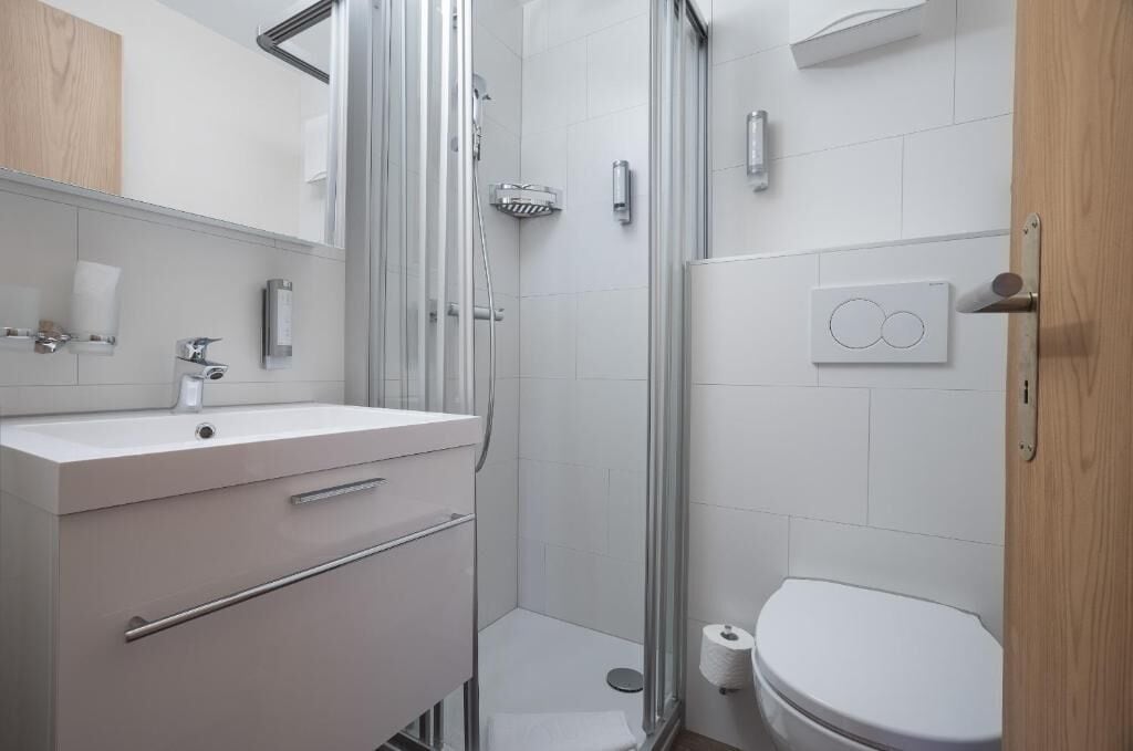 Une salle de bain moderne avec une douche à parois de verre, un lavabo blanc avec un miroir et des toilettes.