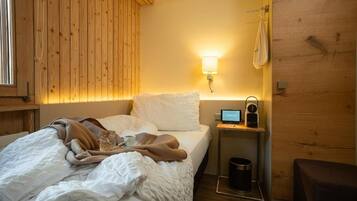 A bedroom with a bed, a bedside table with a lamp, a clock, and a small table with a cup and a glass.