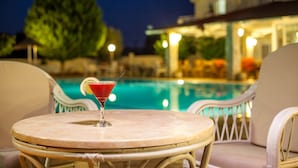 Une table ronde avec un cocktail et une rondelle de citron vert, donnant sur une piscine illuminée la nuit.