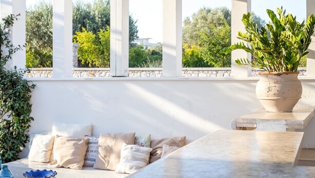 Une pièce baignée de lumière, avec un canapé blanc, des coussins beige, une plante en pot et une table en marbre.
