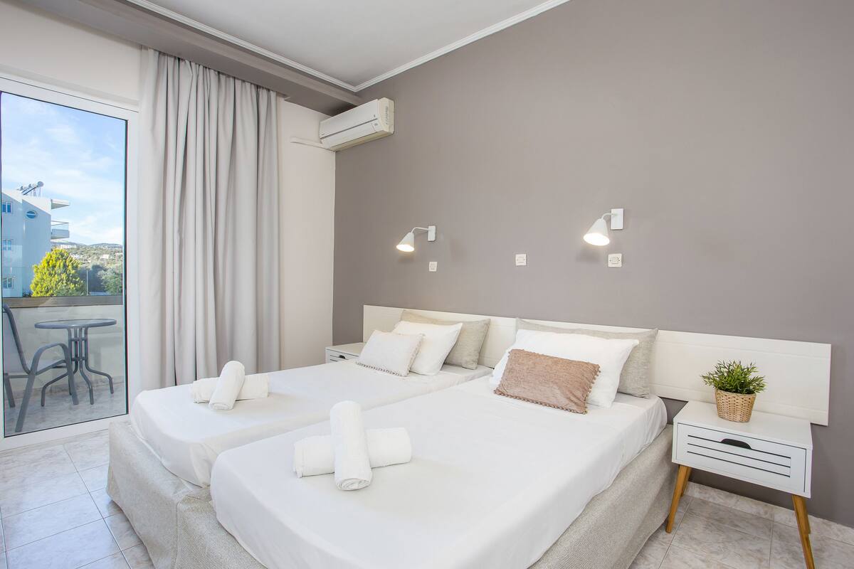 Ein Hotelzimmer mit zwei Betten, einem Balkon und einem weißen Nachttisch mit Pflanze.